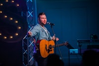a man singing into a microphone with an acoustic guitar
