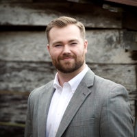 a man in a suit standing in front of a wooden building